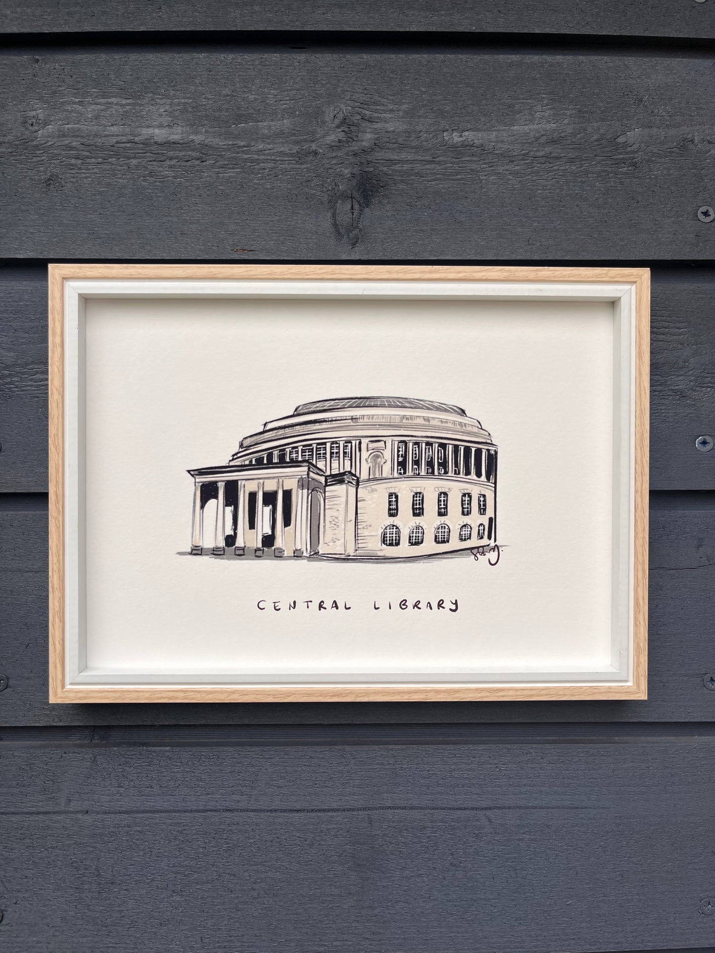 Manchester central library art print, framed in a light wooden frame hung on a wooden dark grey panelled wall