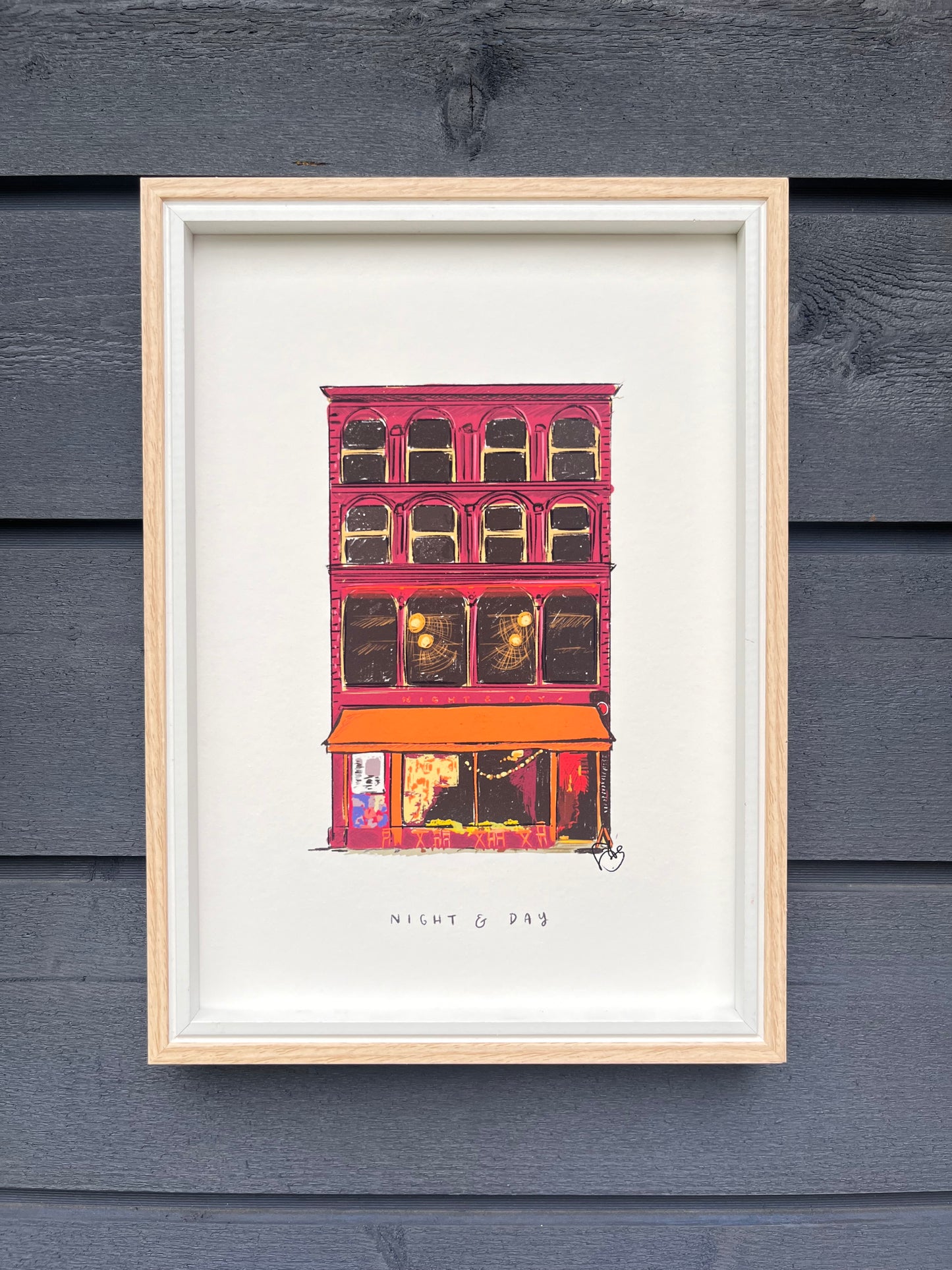 Night and Day venue in Manchester art print, framed in a light wooden frame hung on a wooden dark grey panelled wall
