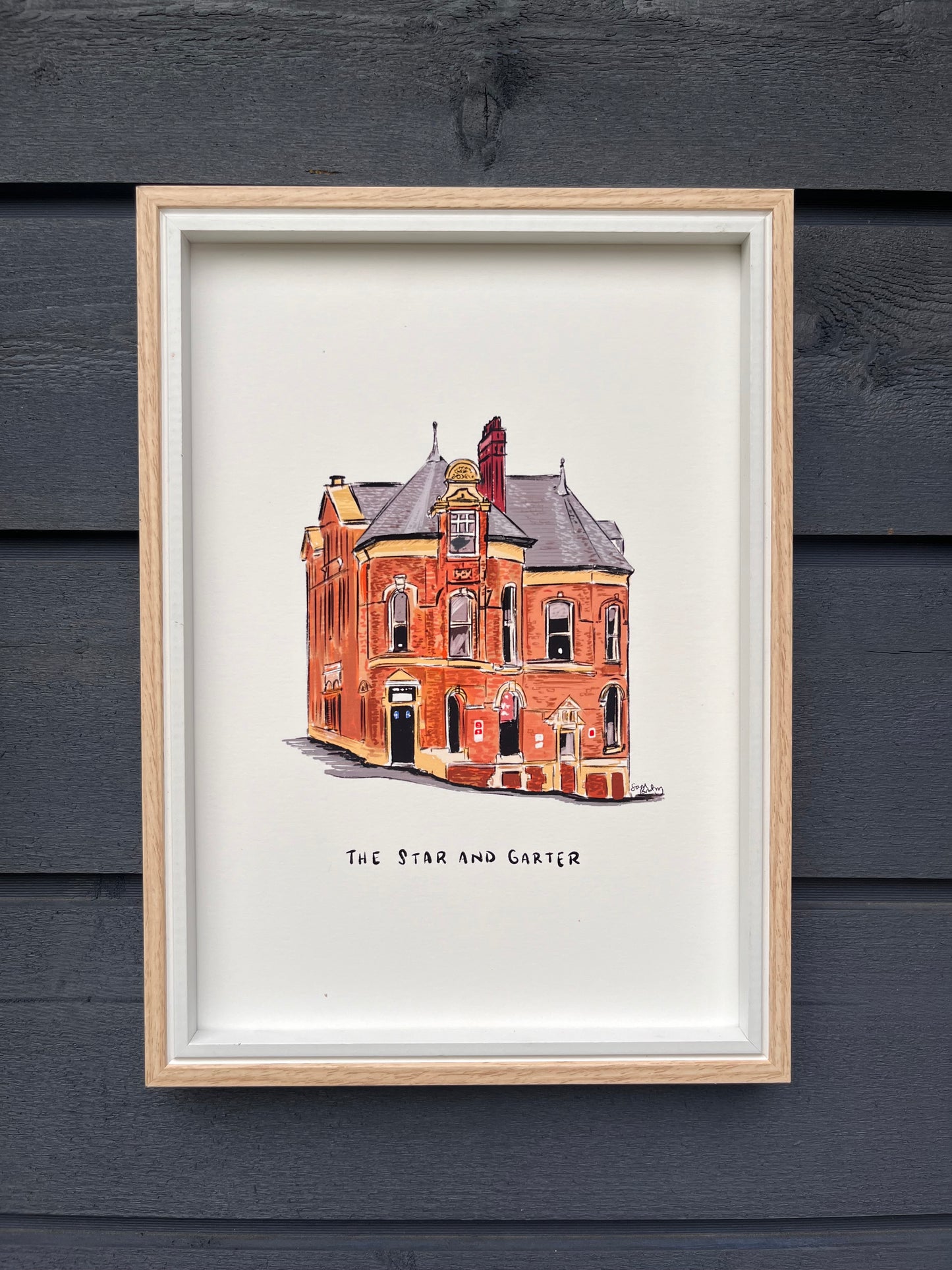 Star and Garter art print, framed in a light wooden frame hung on a wooden dark grey panelled wall